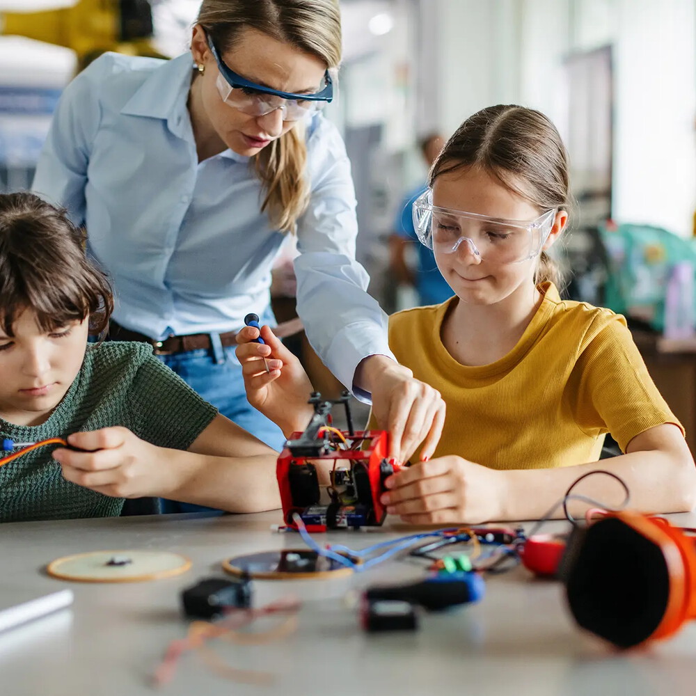 Eine Lehrerin hilft zwei jungen Kindern bei einer technischen Aufgabe im Unterricht