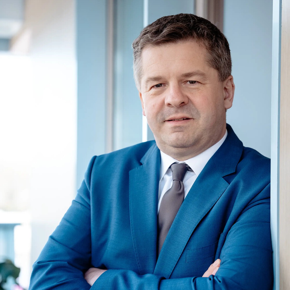 Sven Schulze im blauen Anzug steht lächelnd an eine Wand gelehnt