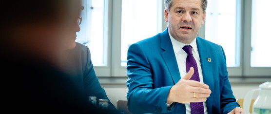 Sven Schulze i Gespräch mit anderen Personen, er sitzt an einem Tisch und hebt die Hand