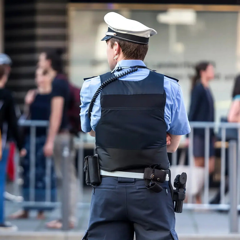 Ein Polizist mit Schussweste und Ausrüstung beobachtet seine Umgebung, Ansicht von hinten